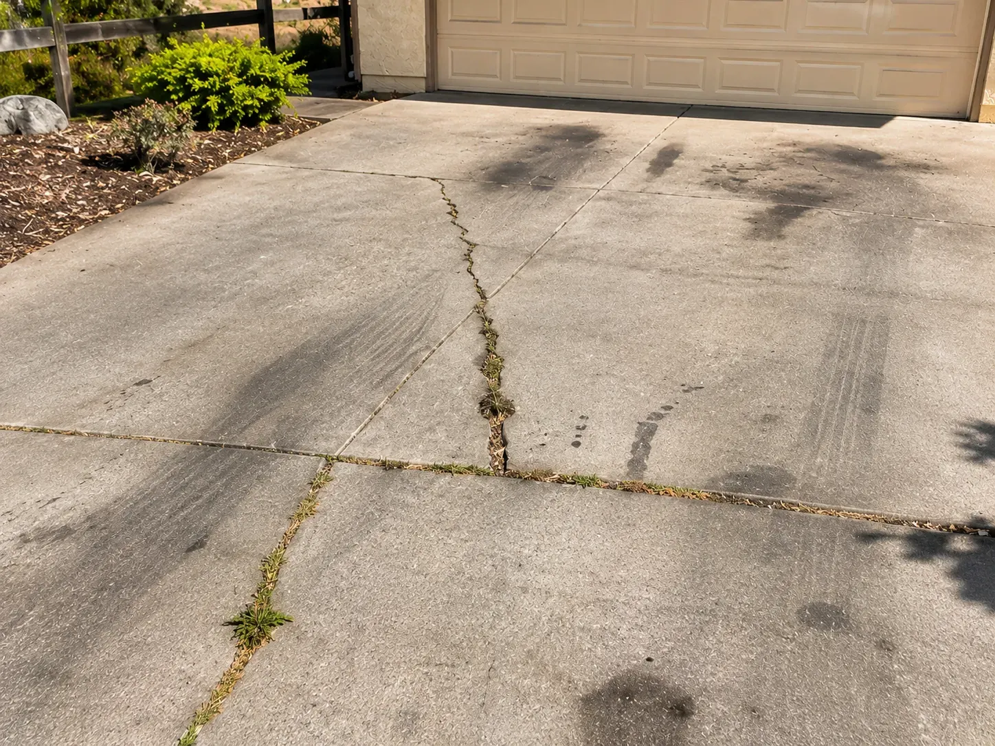 Before: cracked, oil-stained concrete driveway with weeds growing in the cracks