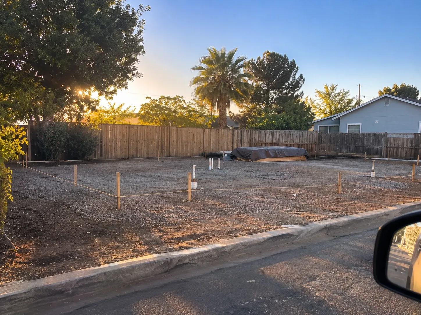 Before: graded gravel building pad staked out with string lines and plumbing stubs