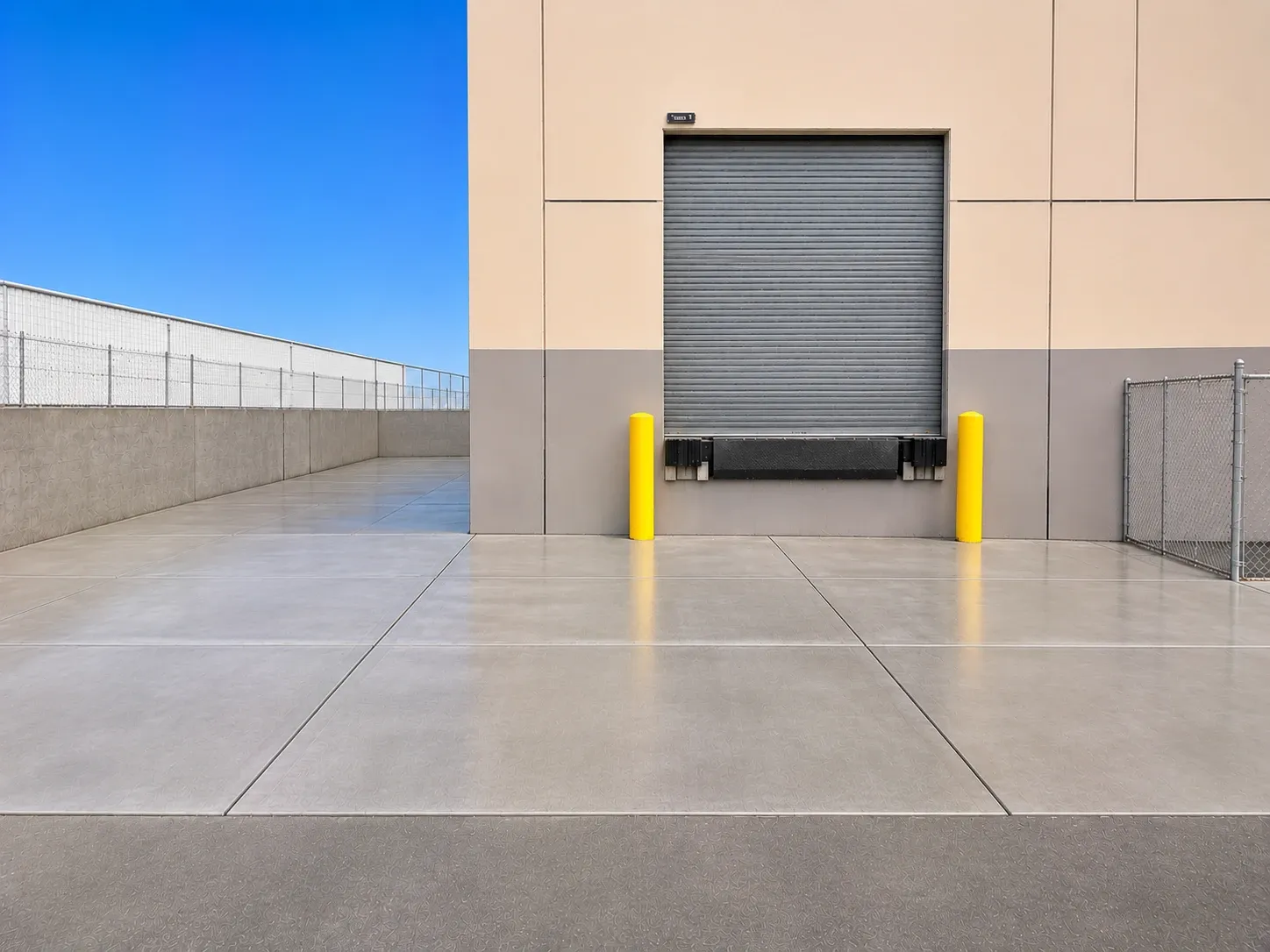 After: a new broom-finished concrete approach slab with saw-cut joints in front of the same warehouse loading dock door and yellow bollards.