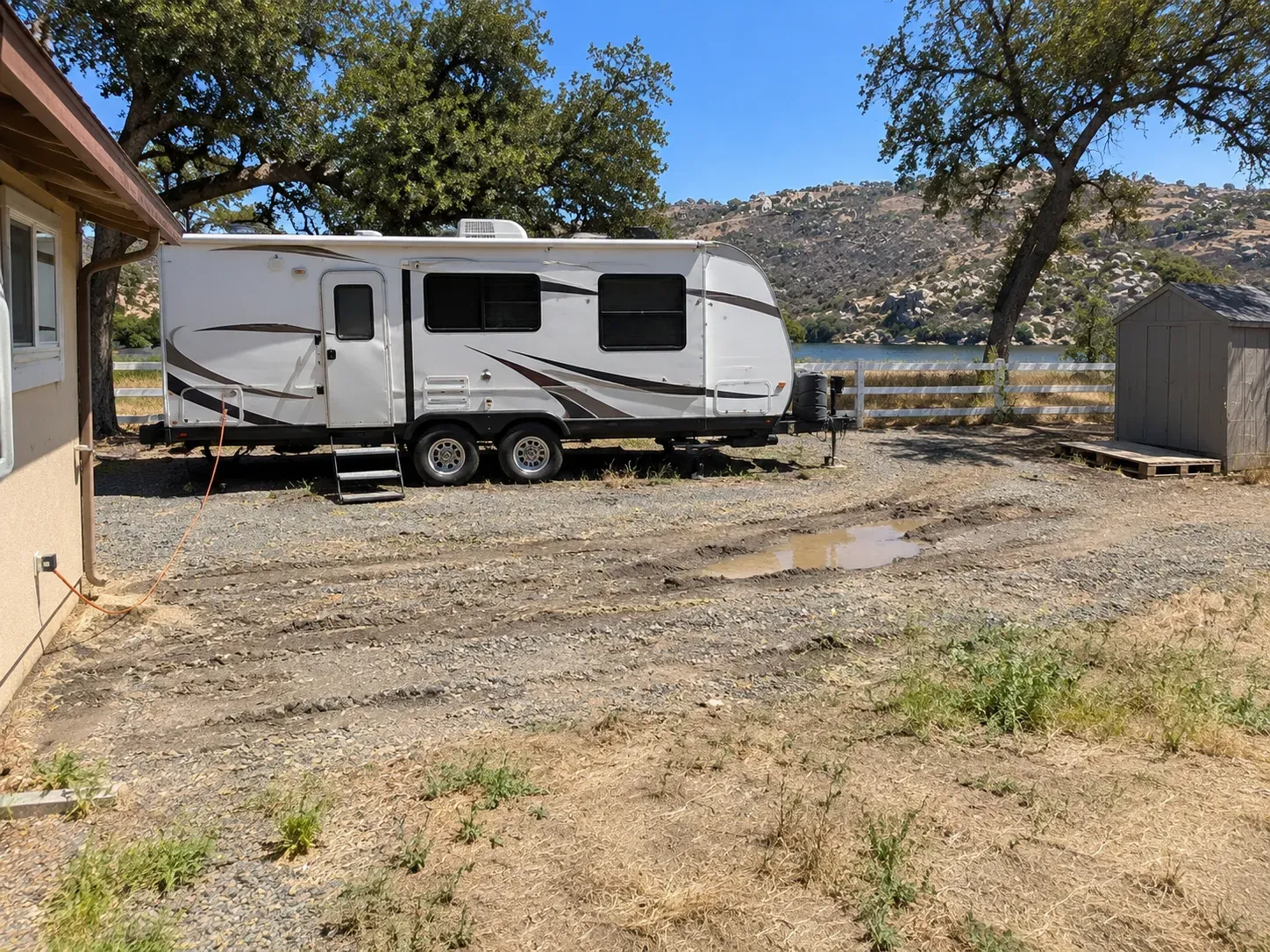 Before: travel trailer parked on rutted, muddy gravel beside the house
